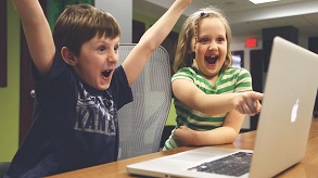 Menino e menina divertem-se em frente ao computador.